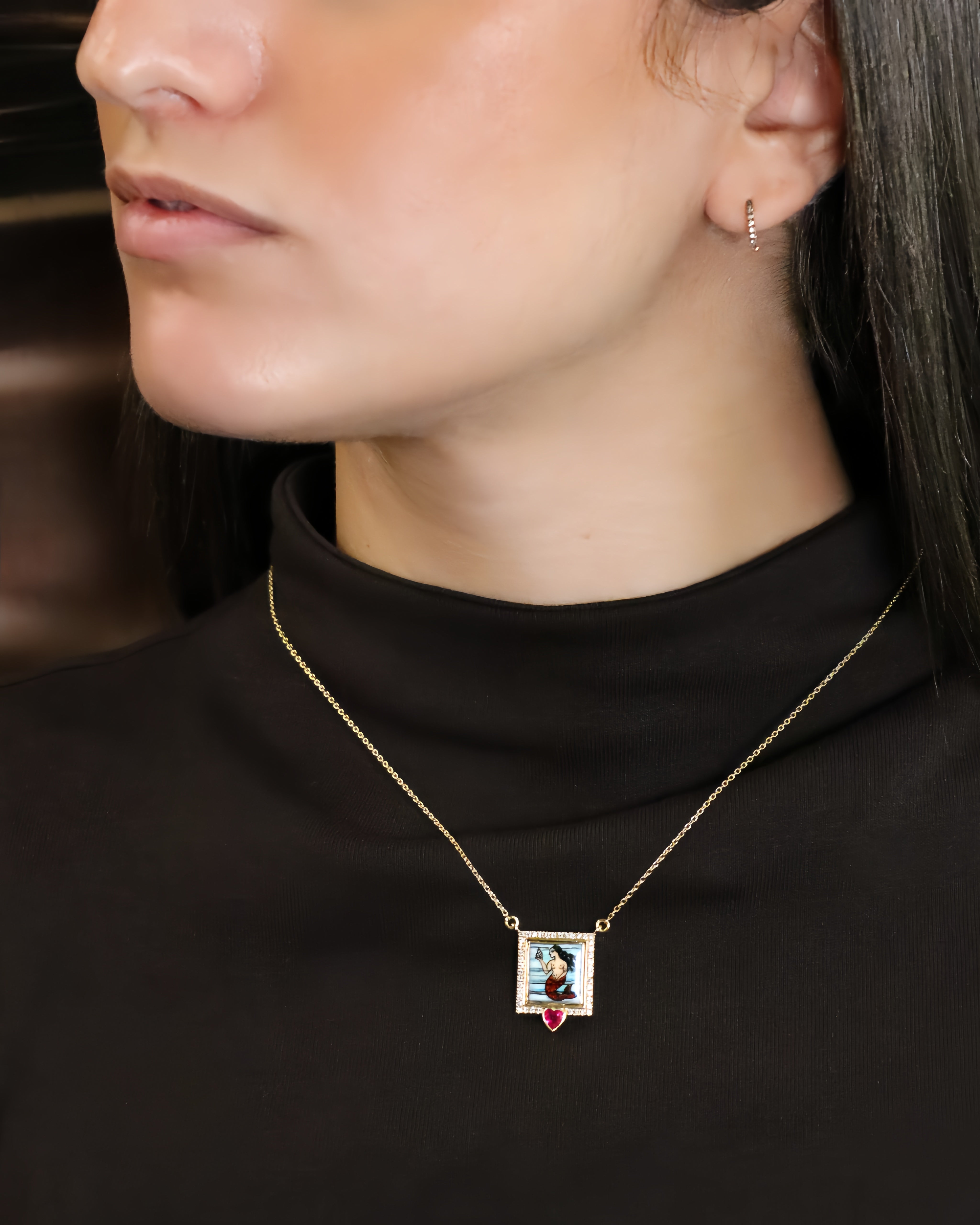 Collana in oro giallo 18K con pendente raffigurante una sirena dipinta a mano in smalto a fuoco, incorniciata da diamanti e arricchita da un rubino a cuore.