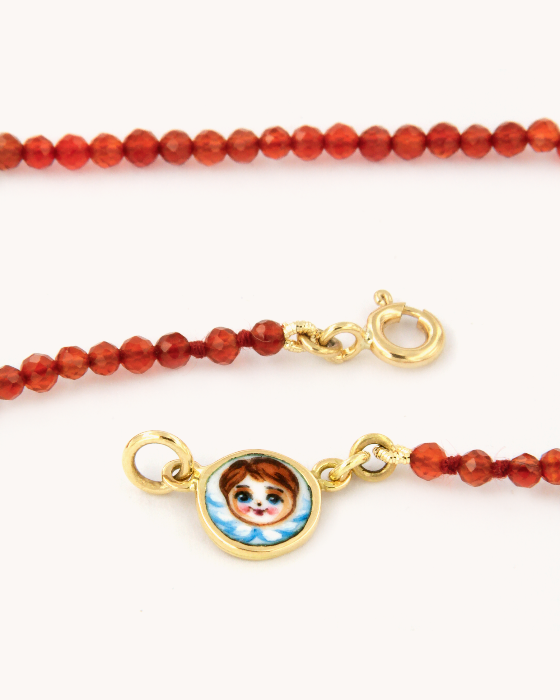 Collana infilata a filo semplice con perline di corniola e chiusura in oro giallo 18 carati, impreziosita da una piastrina decorata con angelo in smalto a fuoco dipinto a mano.