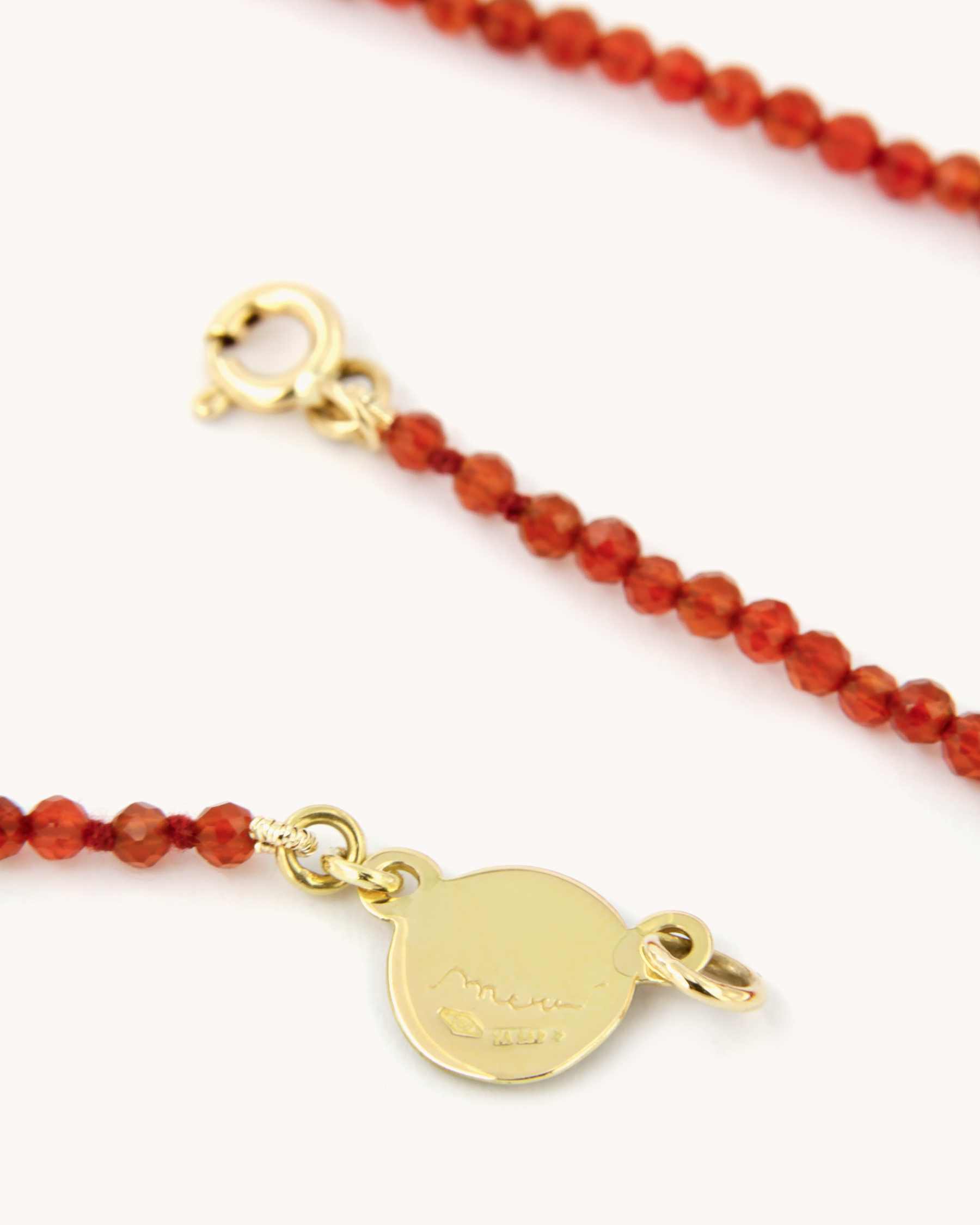 Collana infilata a filo semplice con perline di corniola e chiusura in oro giallo 18 carati, impreziosita da una piastrina decorata con angelo in smalto a fuoco dipinto a mano.