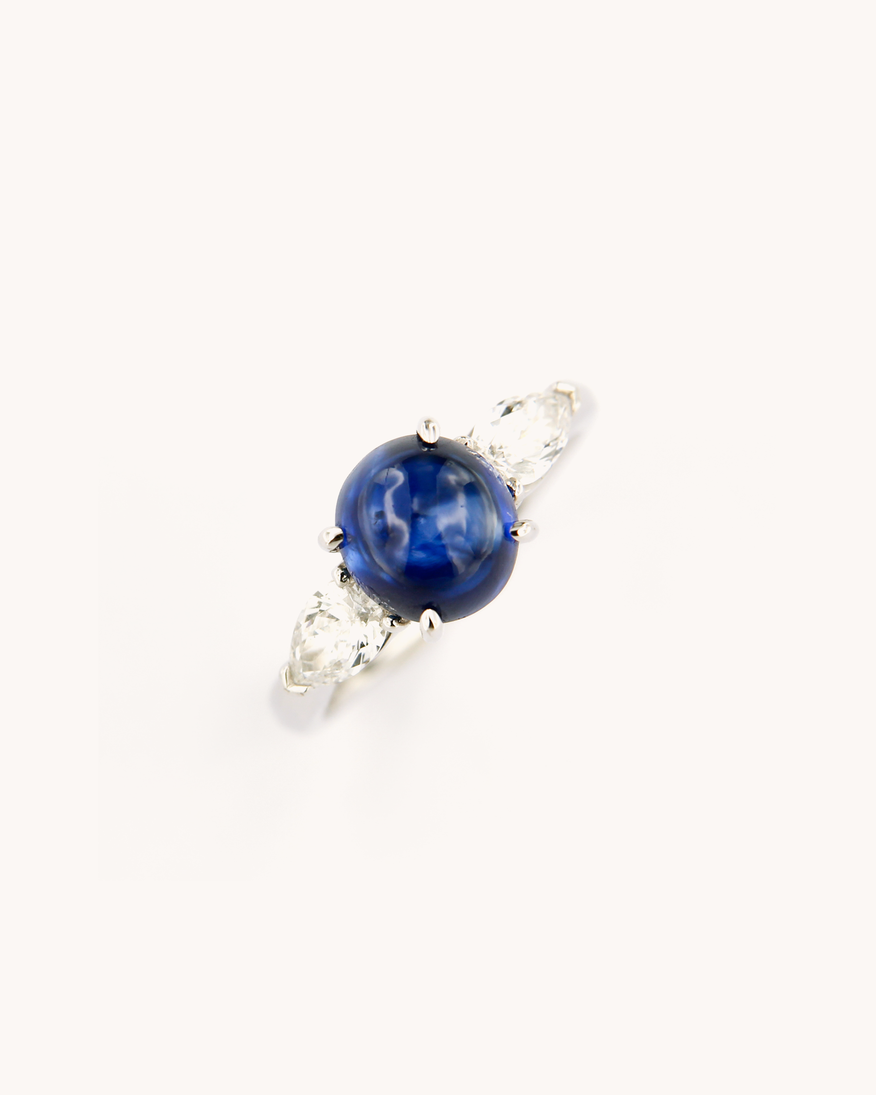 Anello in oro bianco 18K con zaffiro blu cabochon centrale e diamanti laterali taglio marquise.
