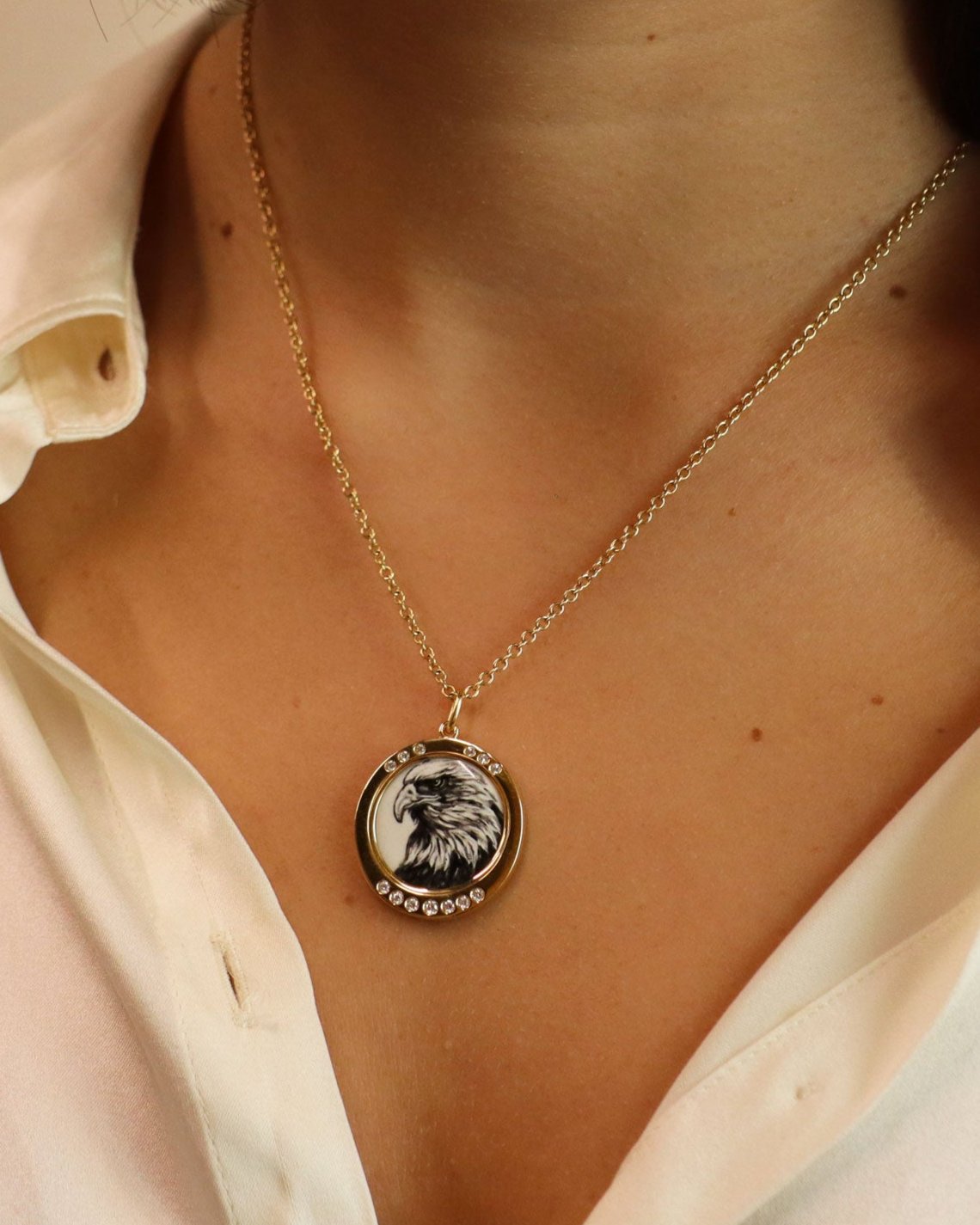 Ciondolo in oro giallo 18K con aquila in smalto a fuoco dipinta a mano e cornice di diamanti bianchi su sfondo blu.