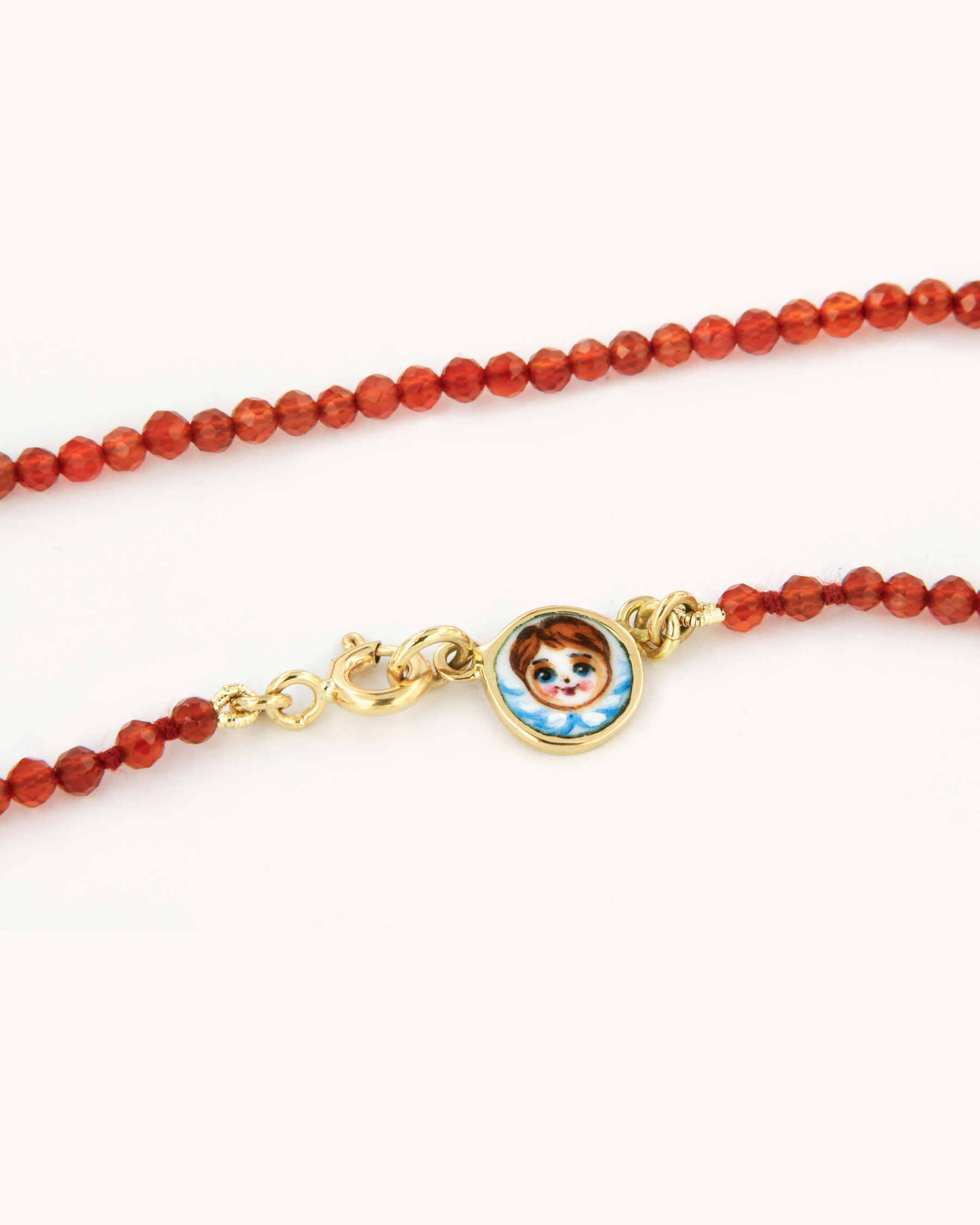 Collana infilata a filo semplice con perline di corniola e chiusura in oro giallo 18 carati, impreziosita da una piastrina decorata con angelo in smalto a fuoco dipinto a mano.