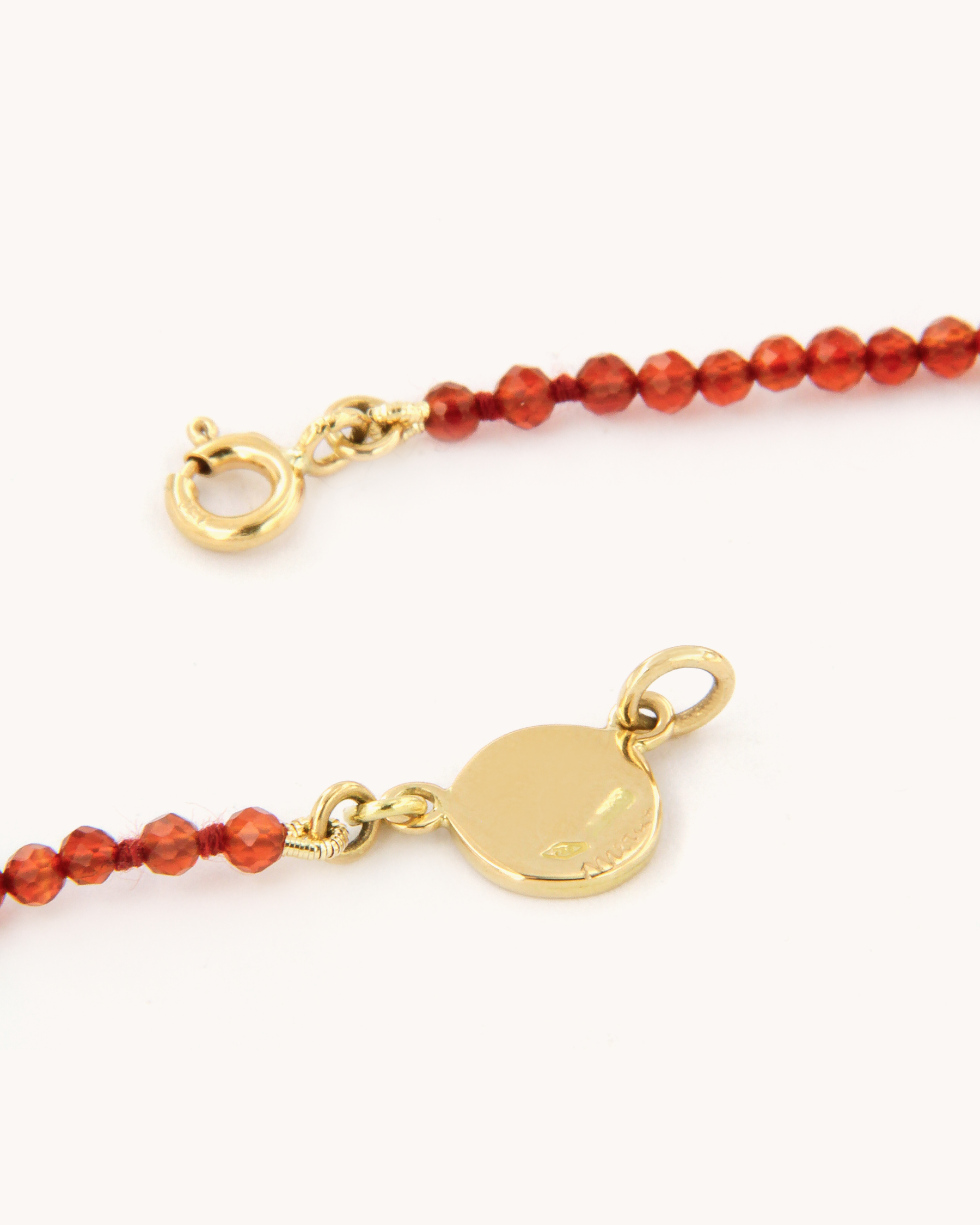 Collana infilata a filo semplice con perline di corniola e chiusura in oro giallo 18 carati, impreziosita da una piastrina decorata con angelo in smalto a fuoco dipinto a mano.