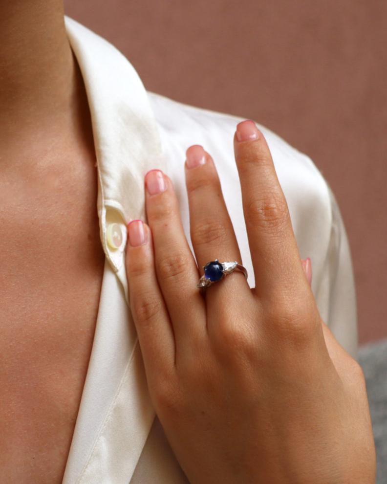 Anello in oro bianco 18K con zaffiro blu cabochon centrale e diamanti laterali taglio marquise.
